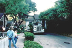 a truck moving a house down the street while people watch