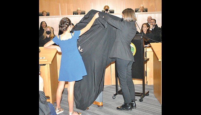 Two girls help Judge Kirk Athanasiou put on his robe.