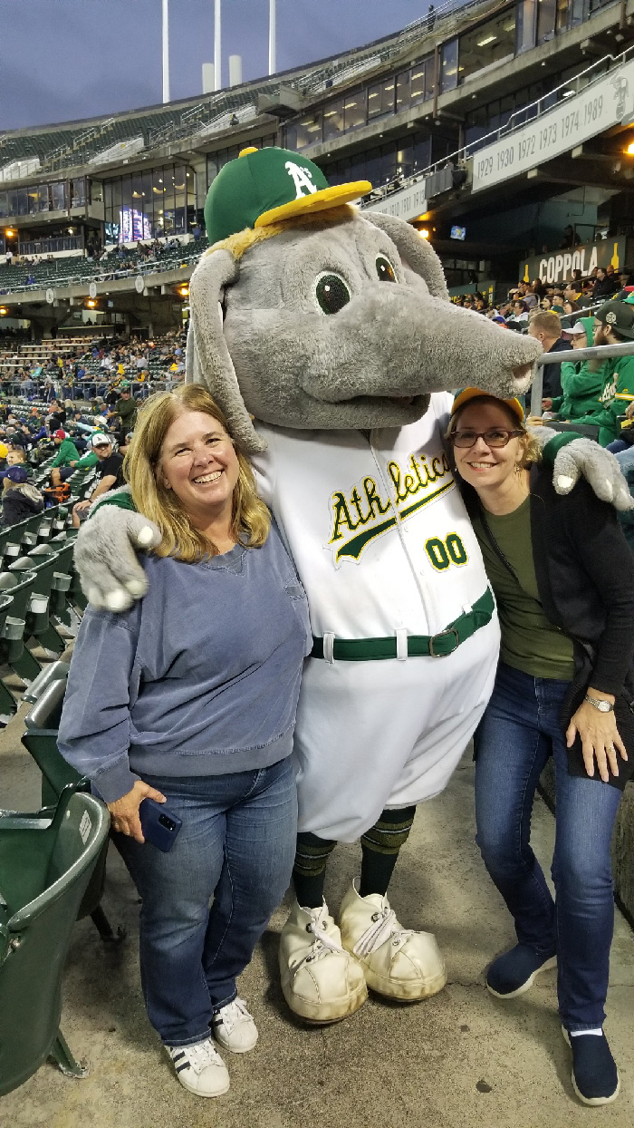 Stomper the A's mascot hugs two women at the A's game in July 2022