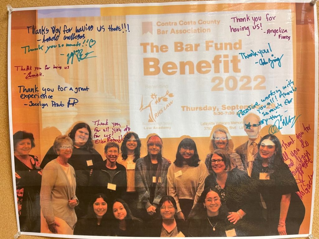 Group of people in front of a slide that reads, The Bar Fund BEnefit 2022, with signatures of students from Richmond High school Law Academy.