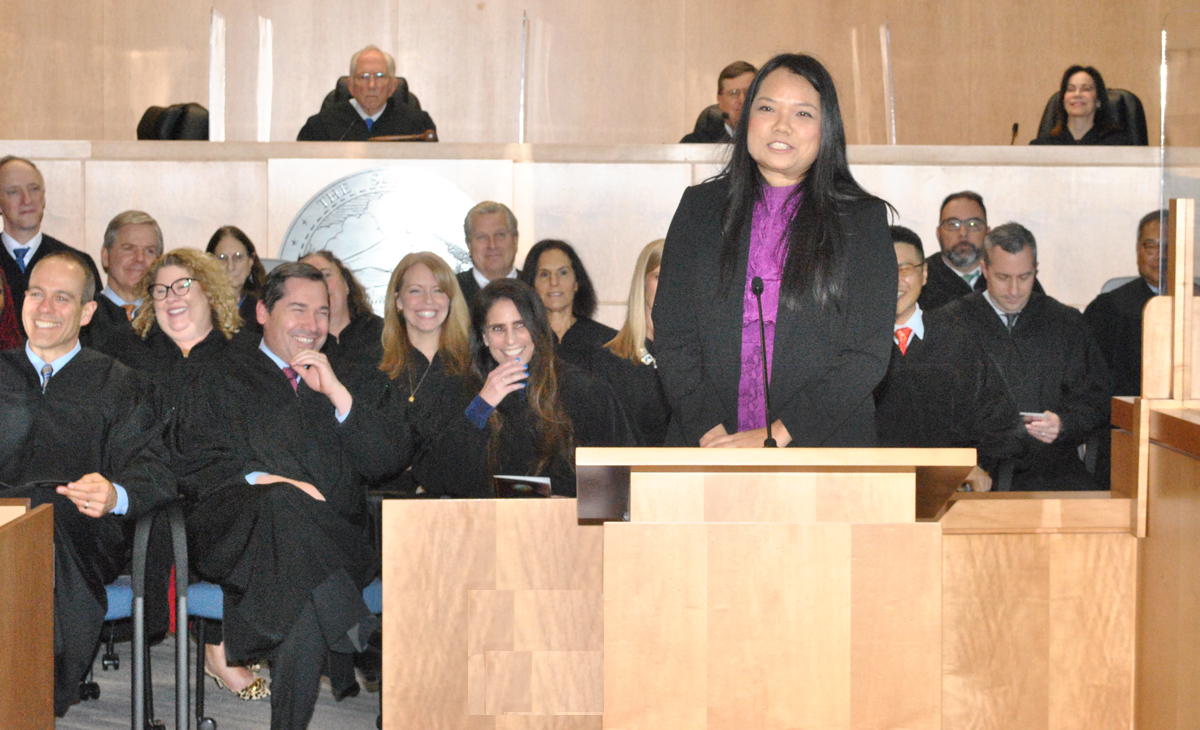Woman speaking from poedium, in front of judges.